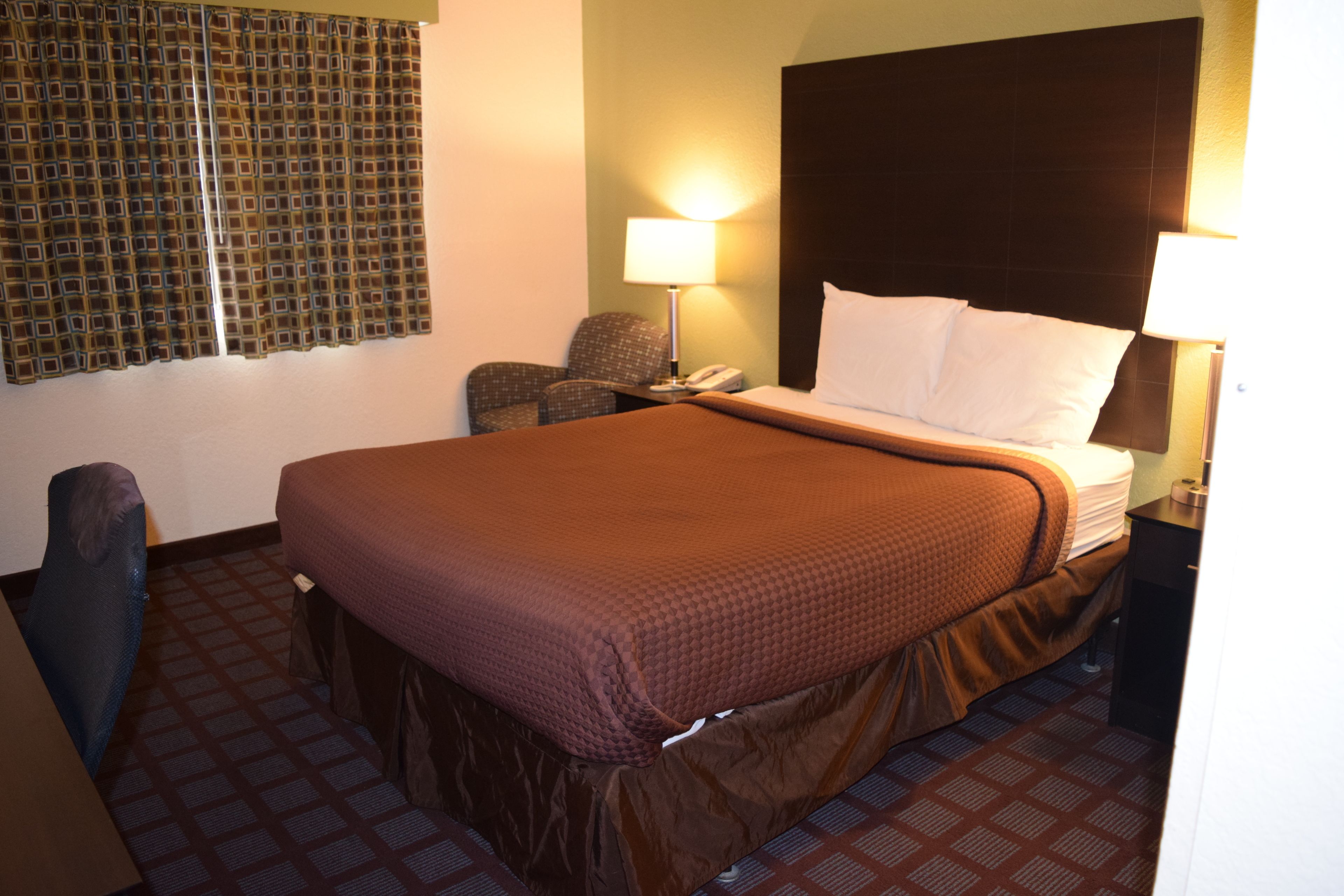 Una habitación de hotel con una cama grande, dos lámparas de noche, una silla y un teléfono.