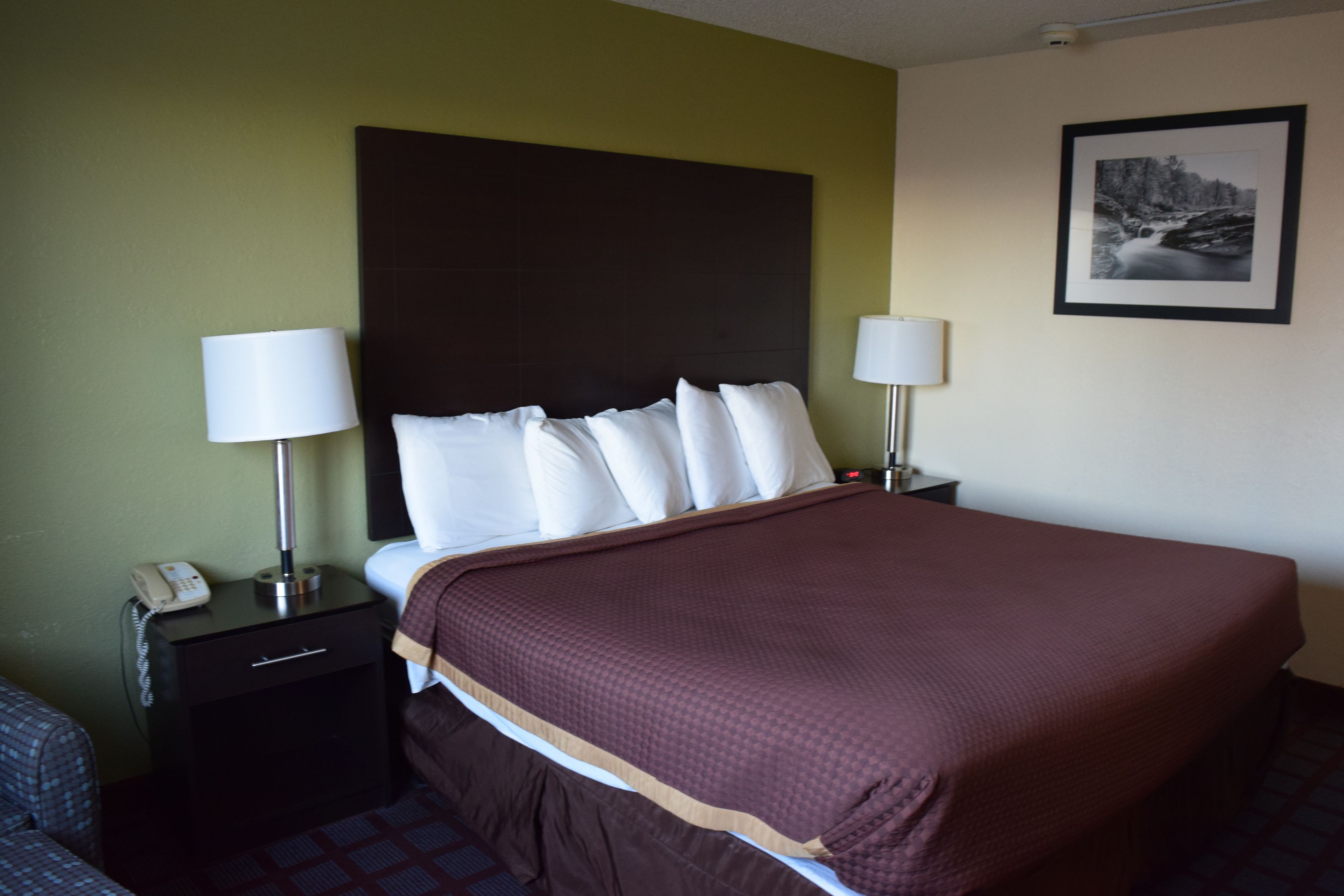 A hotel room with a large bed, two bedside tables with lamps, a nightstand with a phone, and a framed picture on the wall.