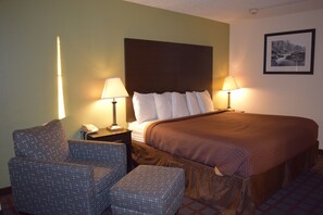 Una habitación de hotel con una cama grande, dos lámparas de noche, una silla y una mesita con un teléfono.