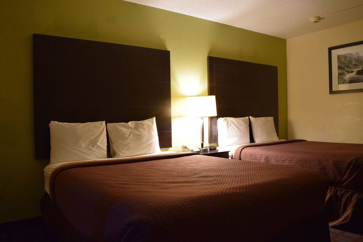 Habitación de hotel con dos camas, una mesita de noche con lámpara y un cuadro enmarcado en la pared.