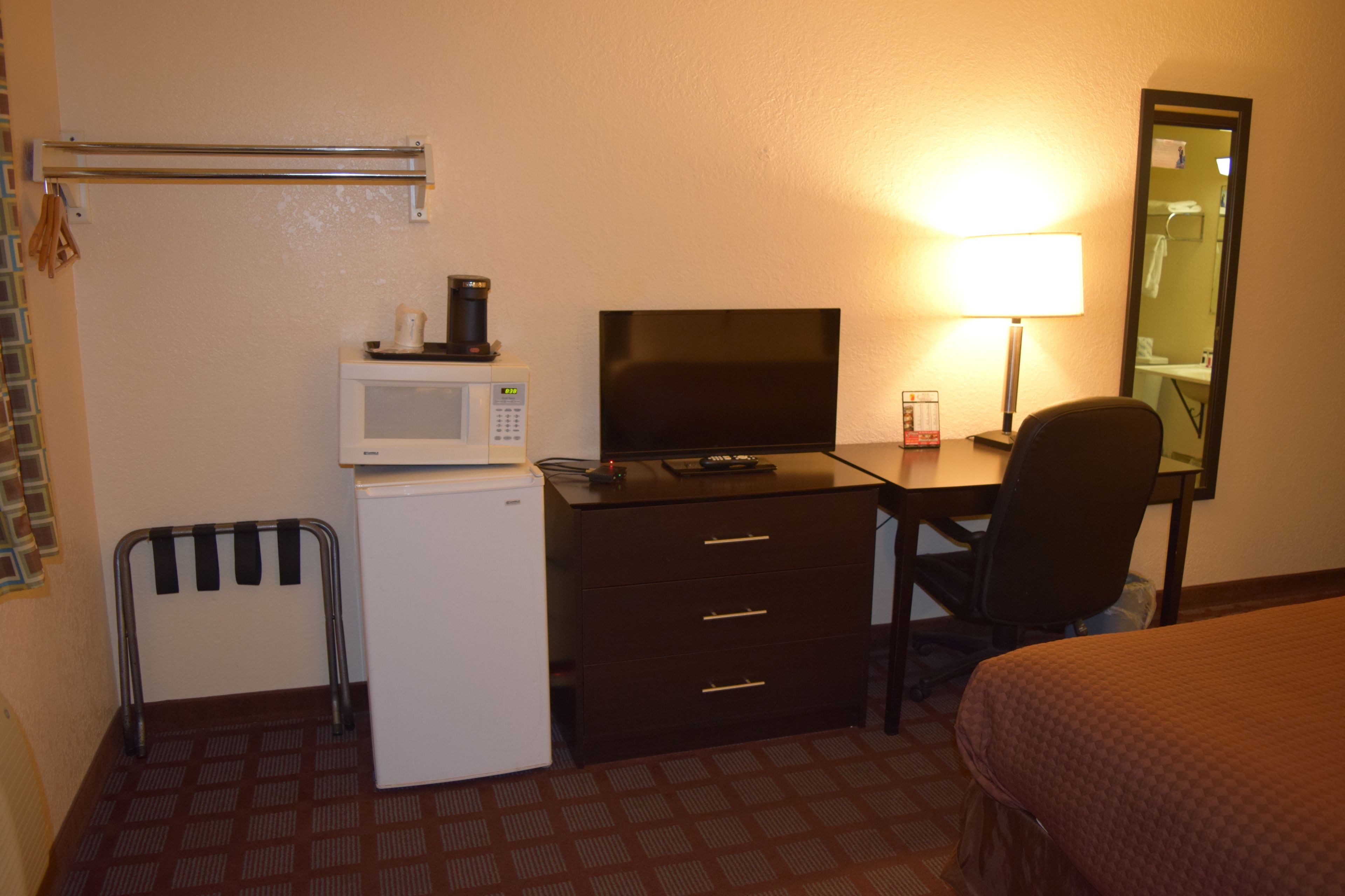 Une chambre d’hôtel comprenant un lit, un bureau avec un ordinateur, un four à micro-ondes, un réfrigérateur, une chaise et une table de chevet avec une lampe.