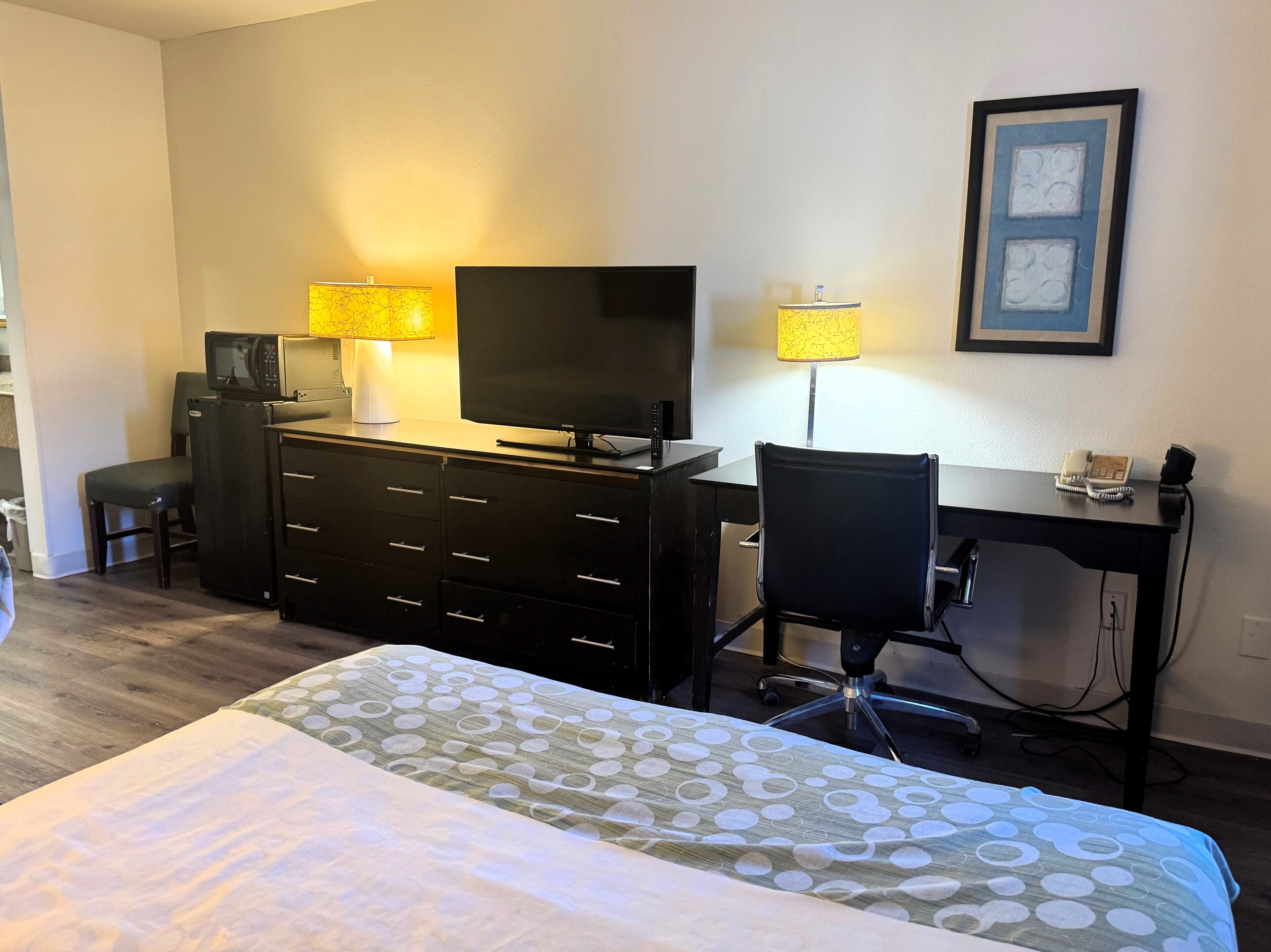 Una habitación de hotel con una cama, un escritorio, una silla, una televisión, un microondas y una lámpara.
