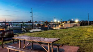 Mesa de piquenique e banco numa área gramada, com um horizonte urbano ao fundo.