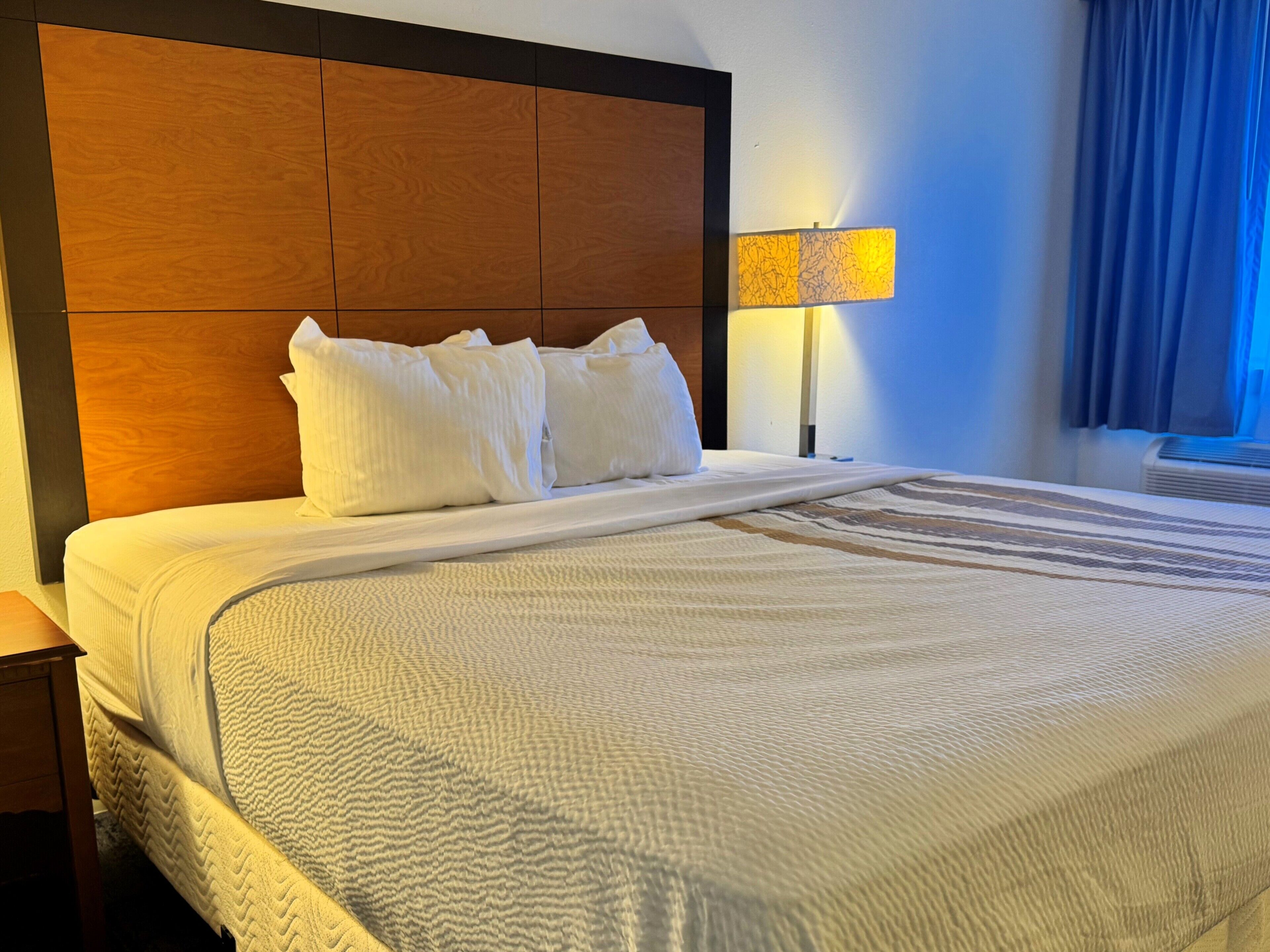 Een hotelkamer met een groot bed, een houten hoofdbord, een bedlampje en een raam met gordijnen.