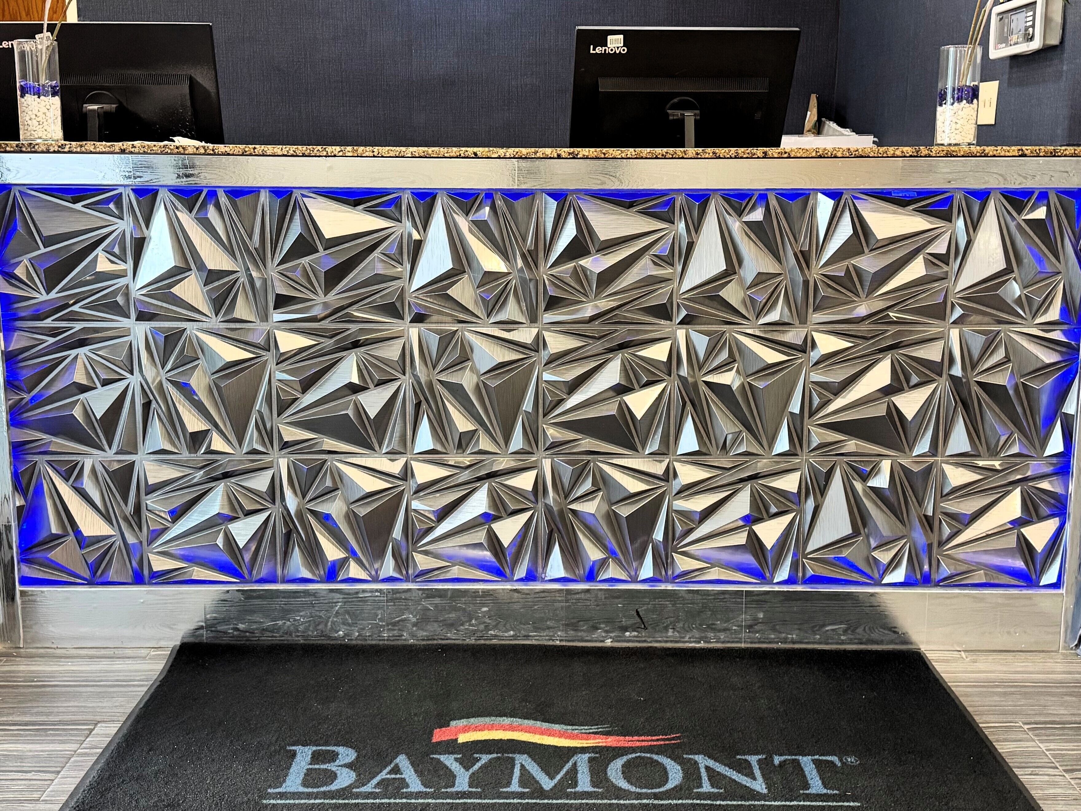 A reception desk with a geometric patterned back wall and a 'Baymont' logo on the carpet.
