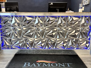 Una recepción con un muro de fondo de diseño geométrico y el logotipo de 'Baymont' en la alfombra.