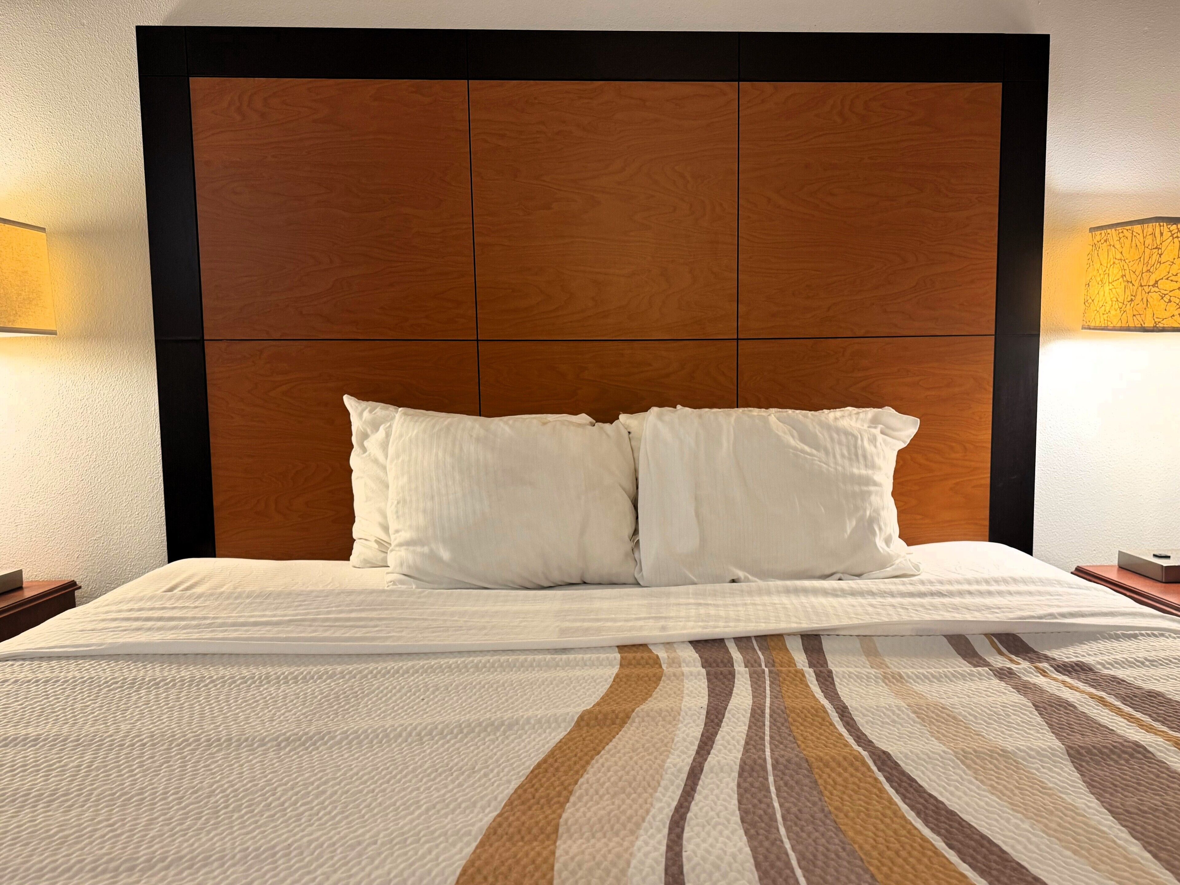 Ein Hotelzimmer mit einem großen Bett, zwei weißen Kissen, einem Holzkopfteil und zwei Nachttischlampen.