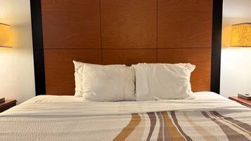 Ein Hotelzimmer mit einem großen Bett, zwei weißen Kissen, einem Holzkopfteil und zwei Nachttischlampen.
