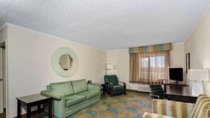 Quarto de hotel com um sofá verde, uma poltrona estampada, uma televisão e uma escrivaninha.