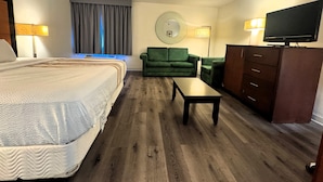 Quarto de hotel com uma cama grande, um sofá verde, uma mesinha, televisão e cómoda.