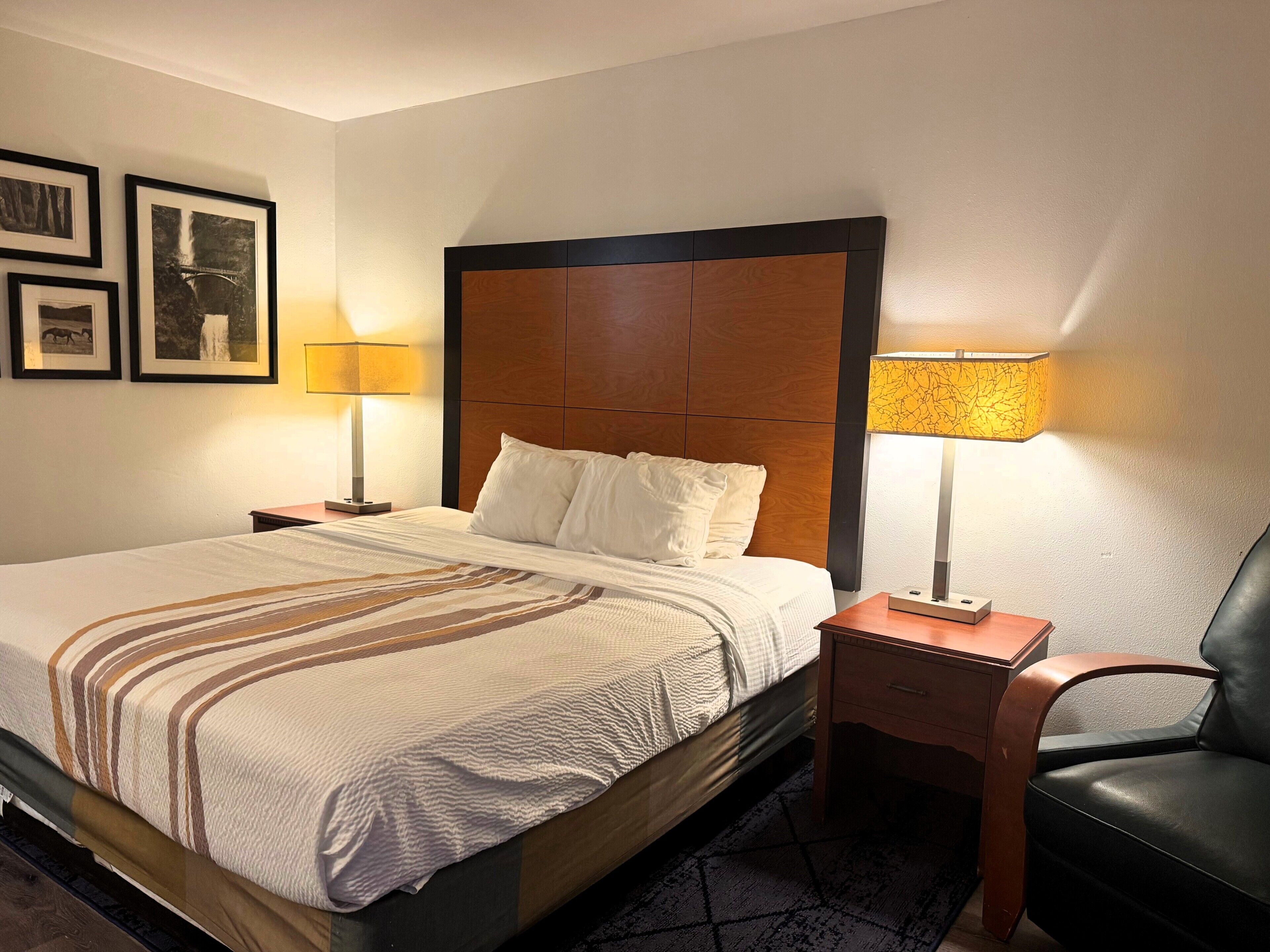 A hotel room with a large bed, two bedside tables with lamps, a chair, and framed pictures on the wall.
