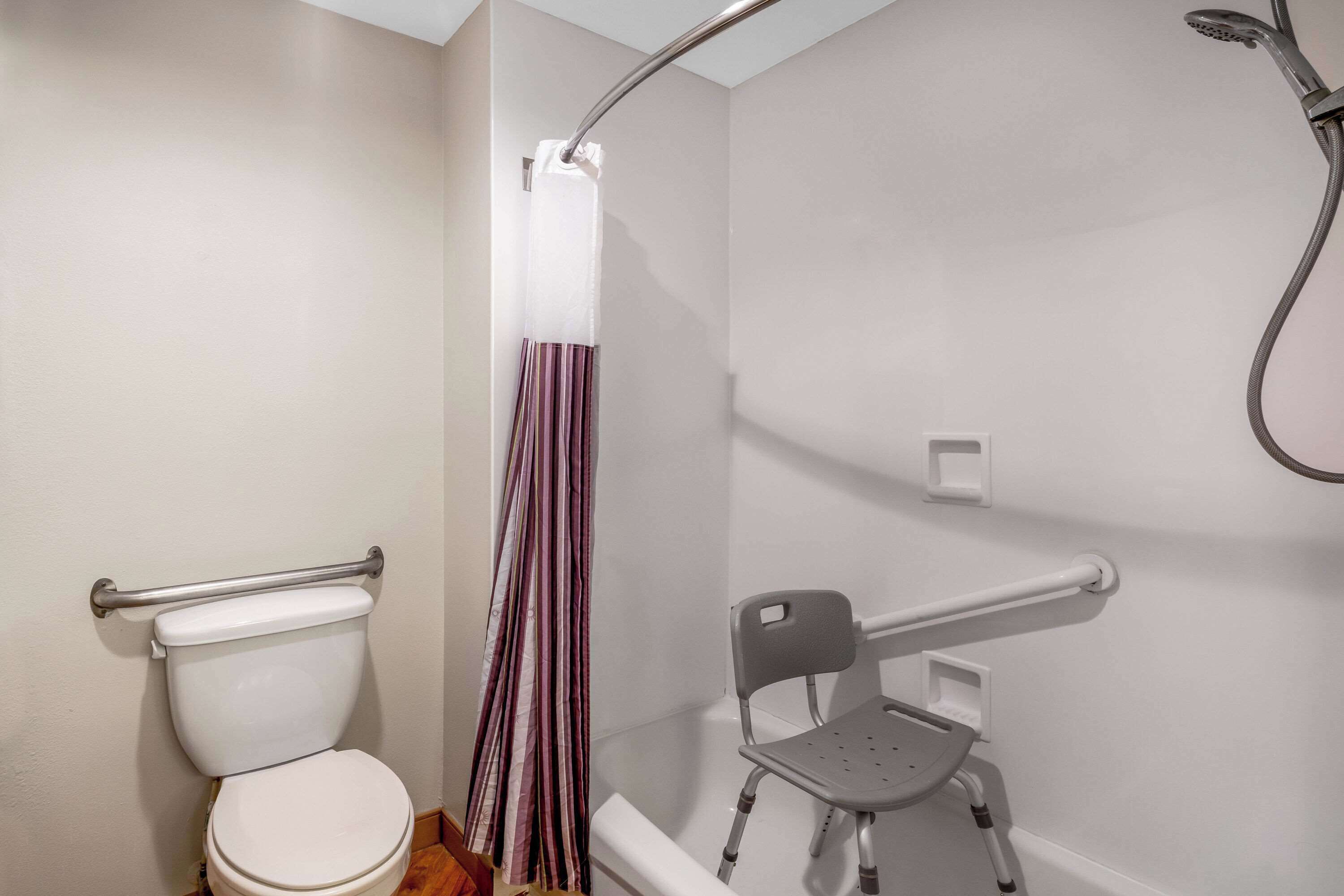 A bathroom with a toilet, shower, and a wheelchair-accessible bench.