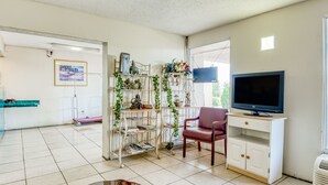 A living room with a TV, a wooden table, a purple chair, a white cabinet, and a decorative shelf with plants and figurines. - OYO Hotel Jackson North I-55 (Jackson)