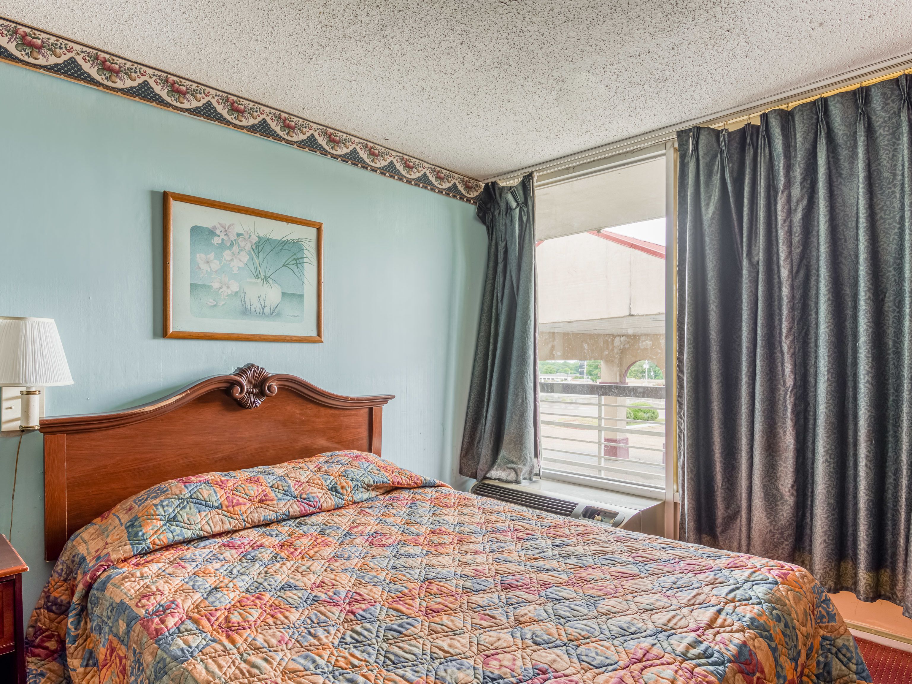 A hotel room with a bed, a framed picture on the wall, and a window with curtains.