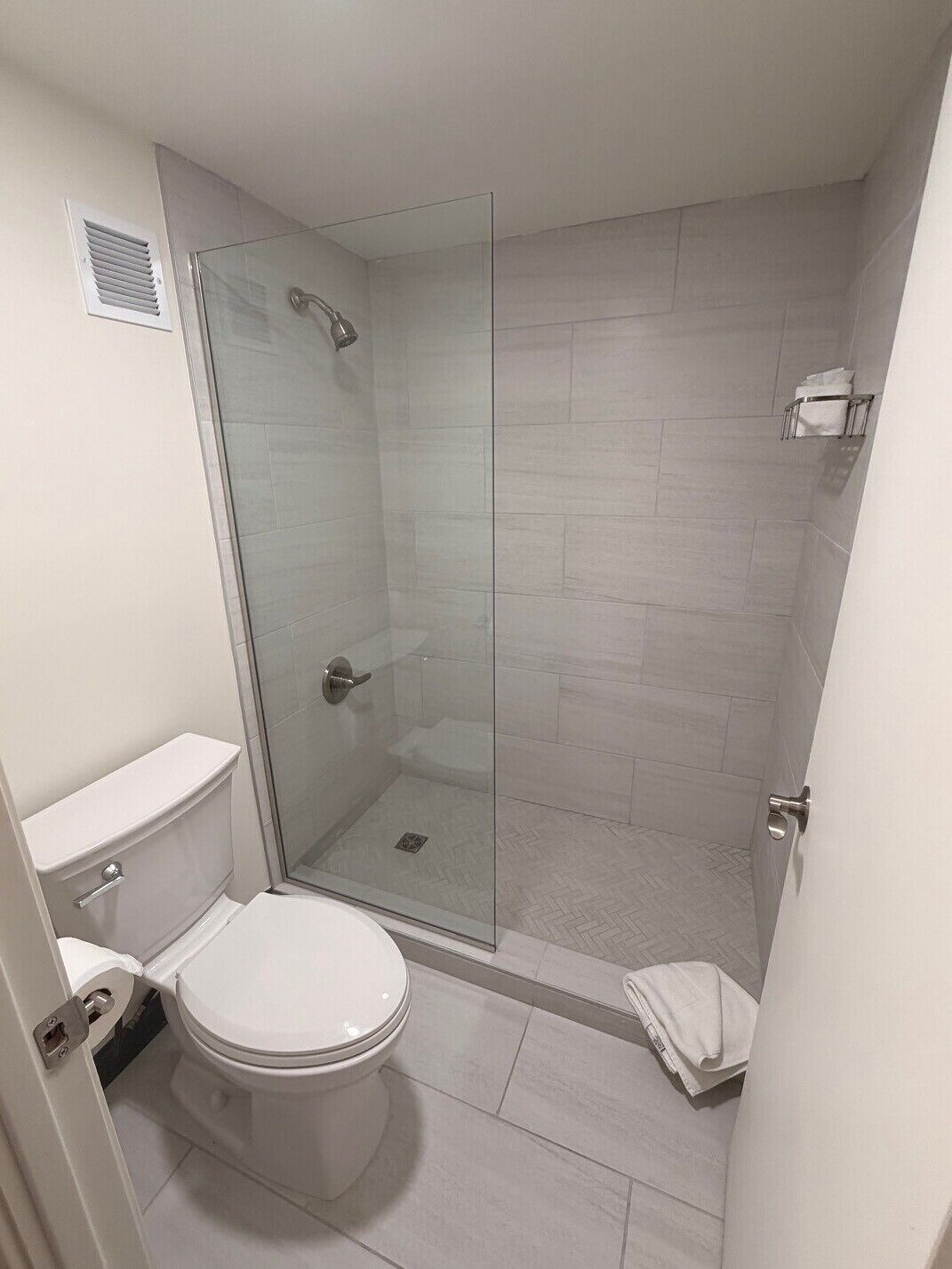 Un baño con inodoro, ducha envuelta en vidrio y piso de baldosas.