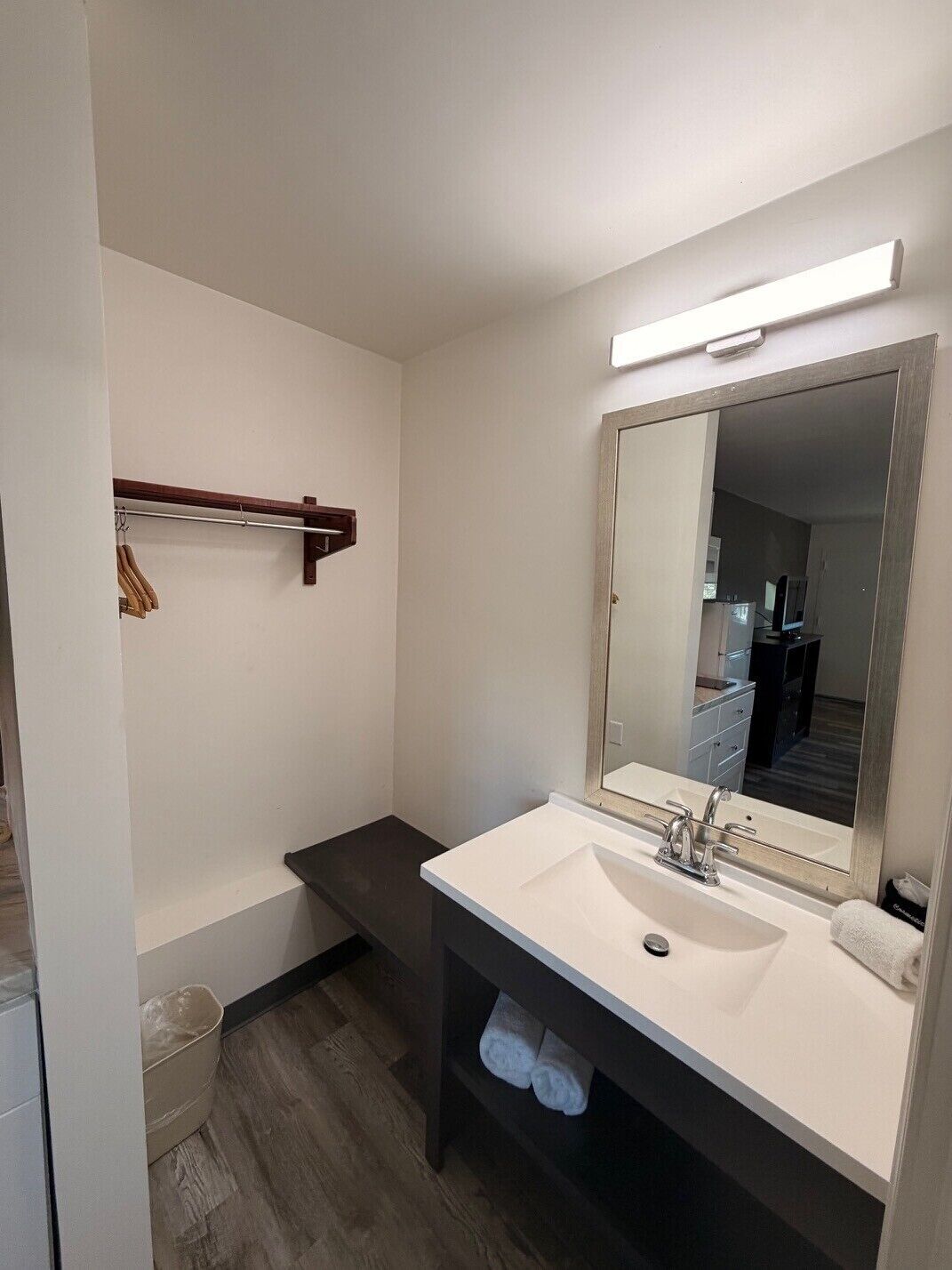 Un bagno moderno con un lavandino bianco, un grande specchio e un portascope legno.