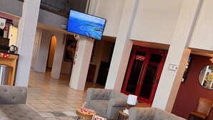A spacious lobby with grey sofas, a flat-screen TV, and a red door indicating a restaurant. - Mariposa Hotel (Nogales)