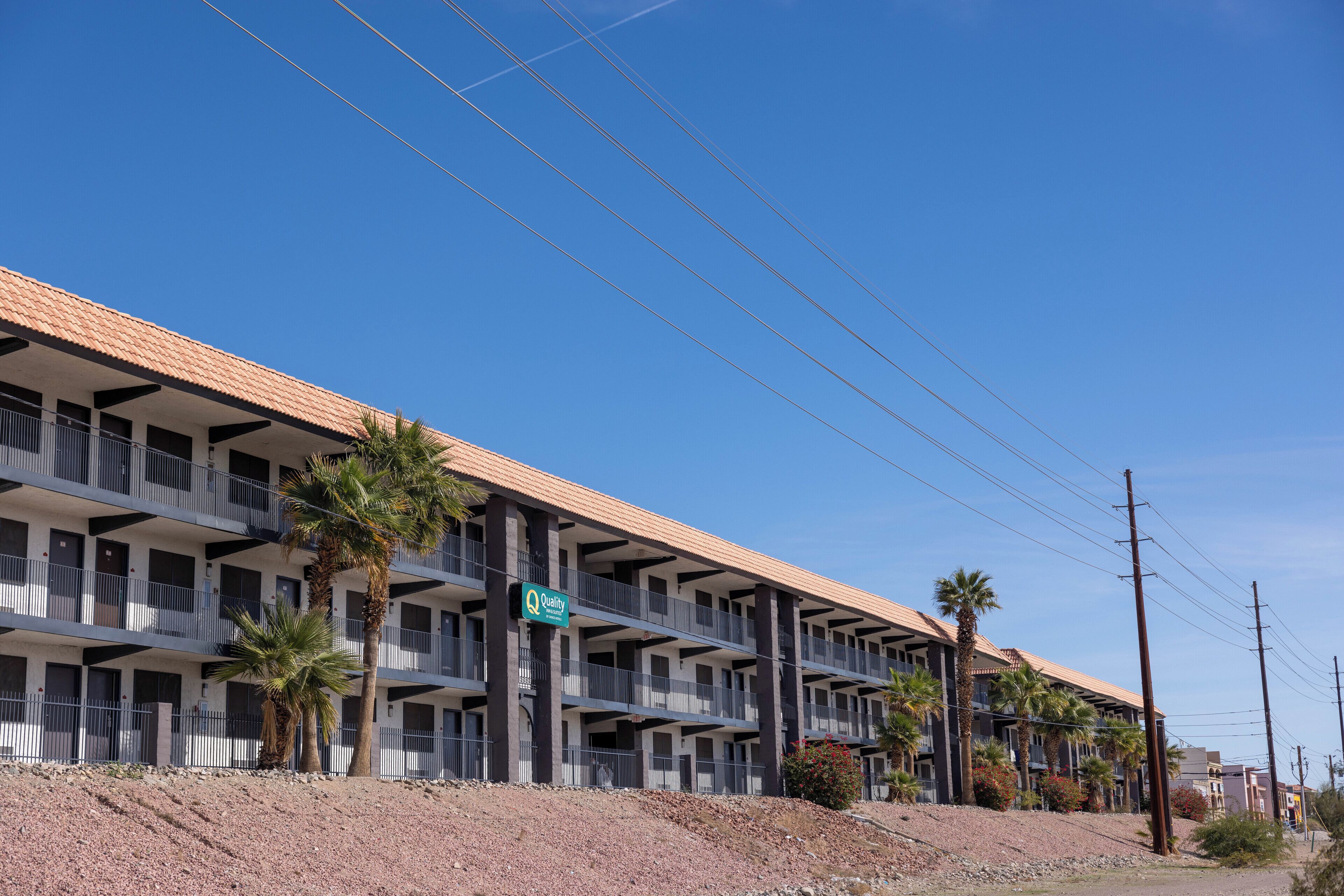 Un motel de varios pisos con techo plano y balcones, situado en terreno rocoso con palmeras.