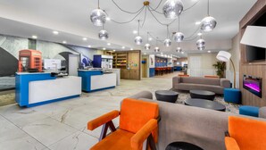 A modern hotel lobby with a reception desk, seating area, and a bar.