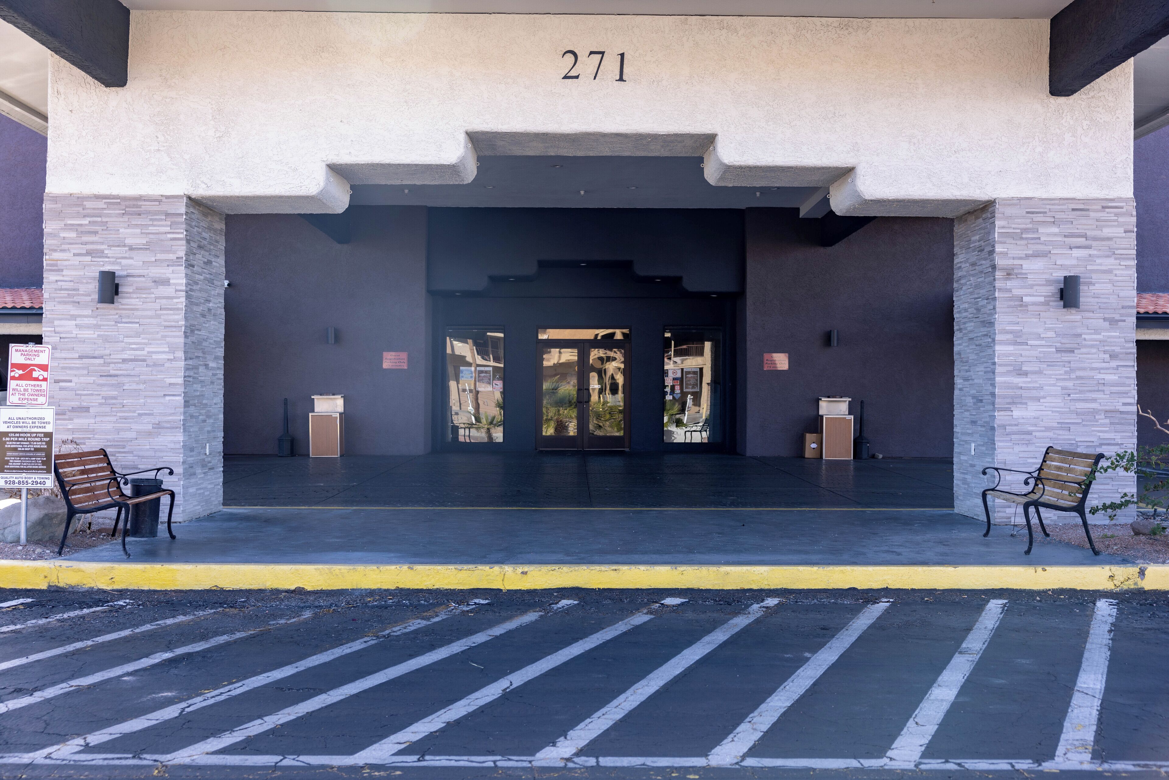 Entrada de un edificio con el número "271" sobre la puerta, dos bancos a cada lado y una borda amarilla en el frente.