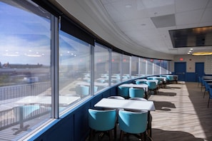 A modern restaurant with a long counter, blue chairs, and large windows offering a view of the city.