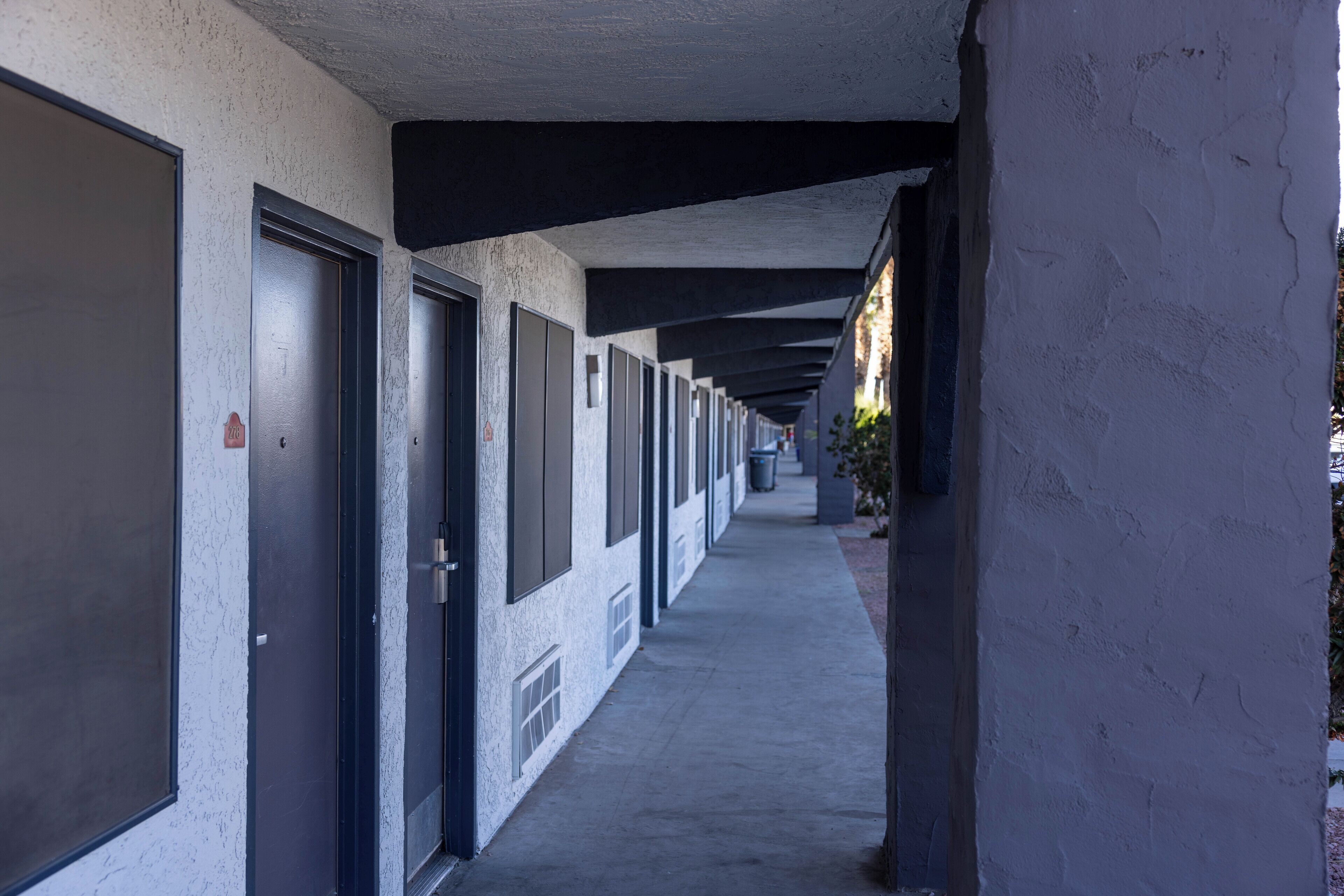 Um corredor com portas de acesso a quartos, piso de concreto e parede branca com textura.