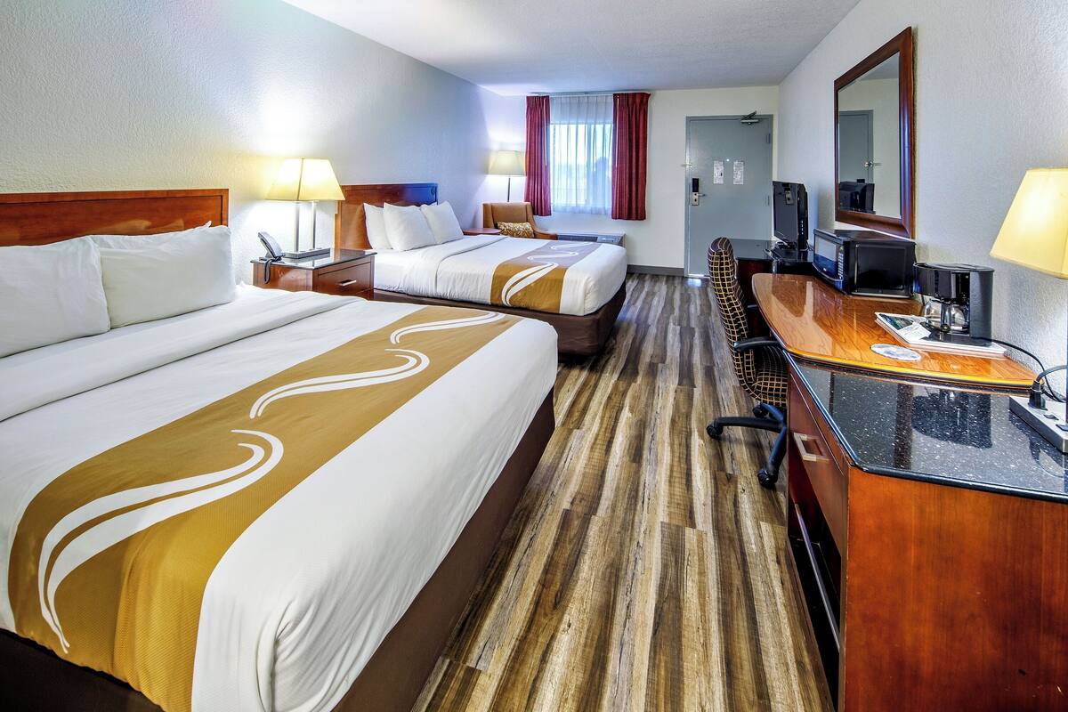 A hotel room with two beds, a desk with a computer, a TV, and a coffee maker.