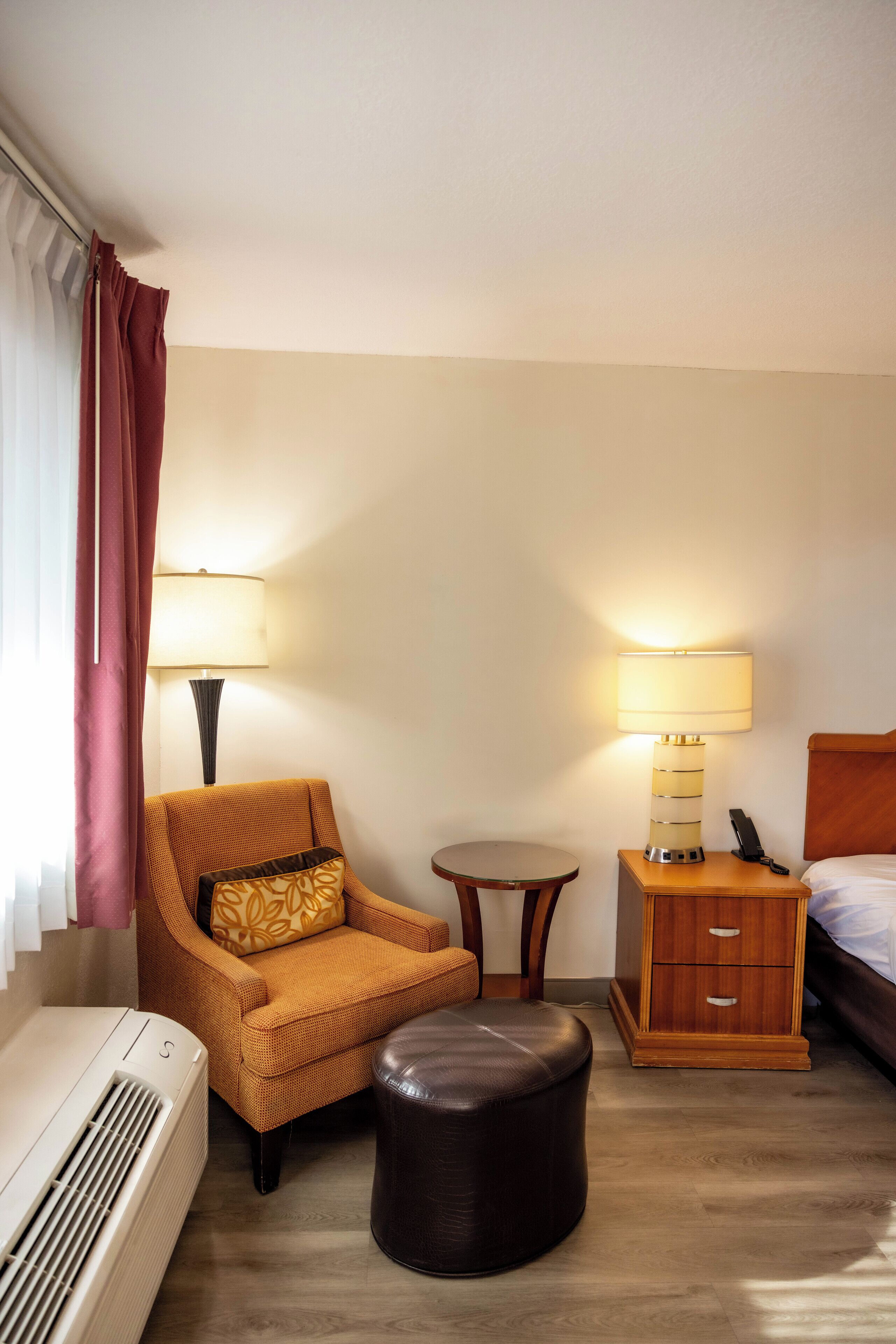 Une chambre d’hôtel comprenant un canapé, une petite table ronde, une table de chevet avec une lampe, un lit et un appareil de climatisation.