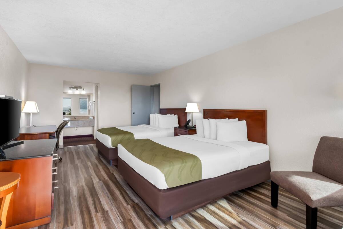 A hotel room with two beds, a desk, a TV, and a chair.