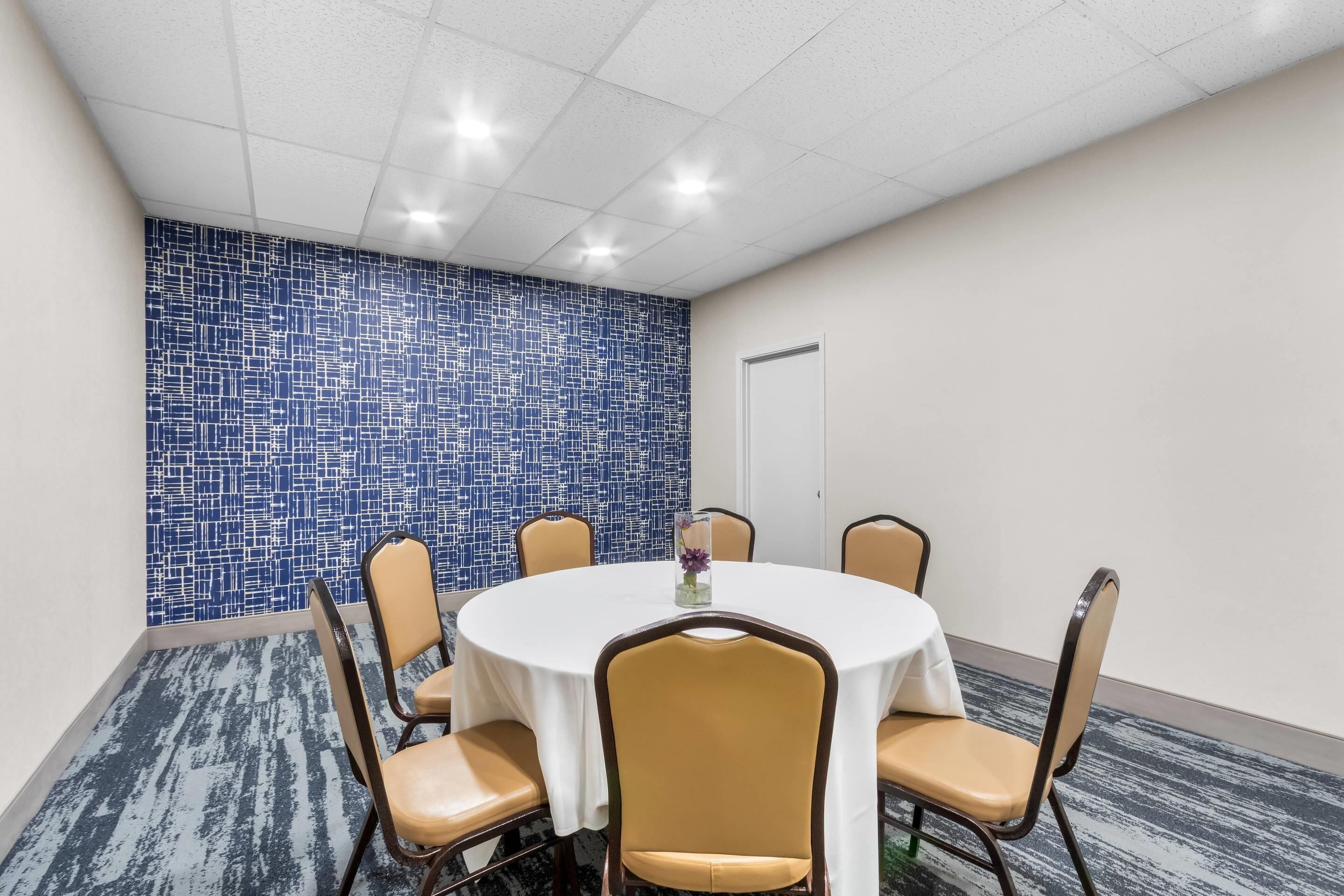 A conference room with a round table, six chairs, and a blue mosaic wall.
