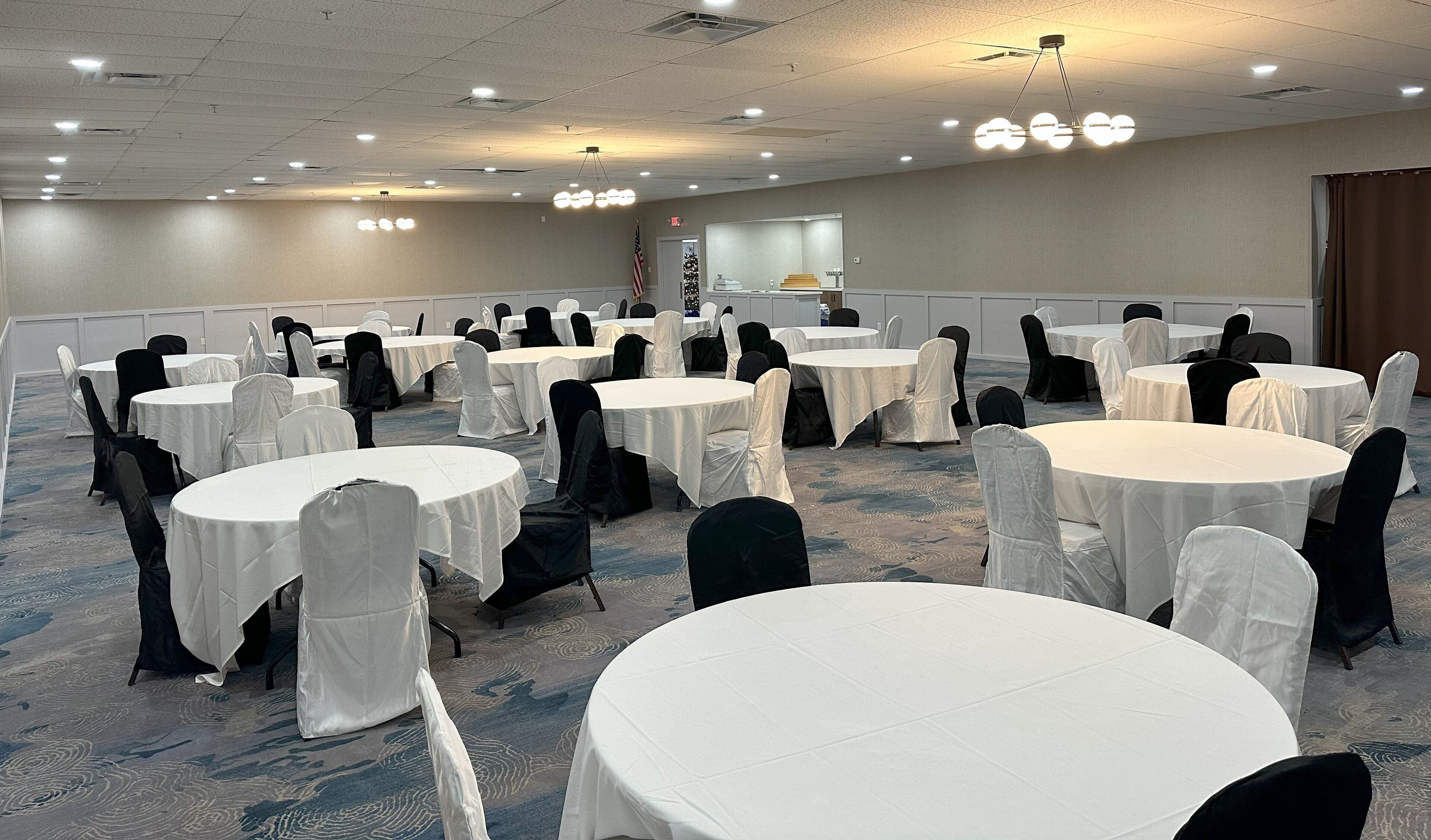 A conference room with round tables covered in white tablecloths, black chairs, and a carpeted floor.