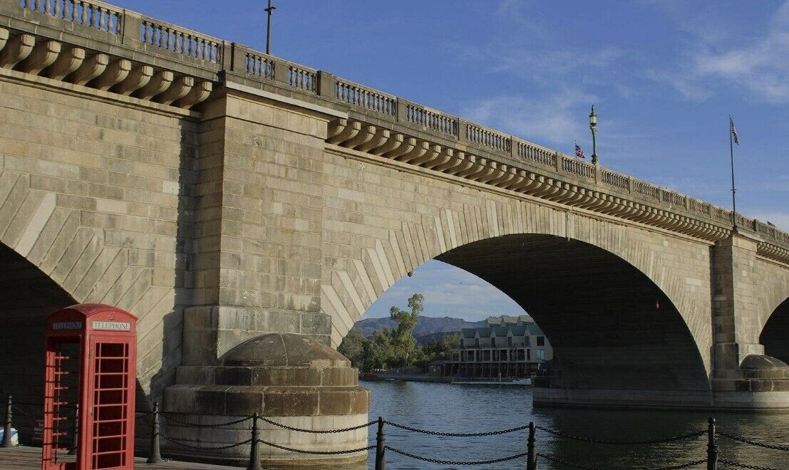 A stone bridge with multiple arches over a body of water, a red telephone booth, and a chain barrier.