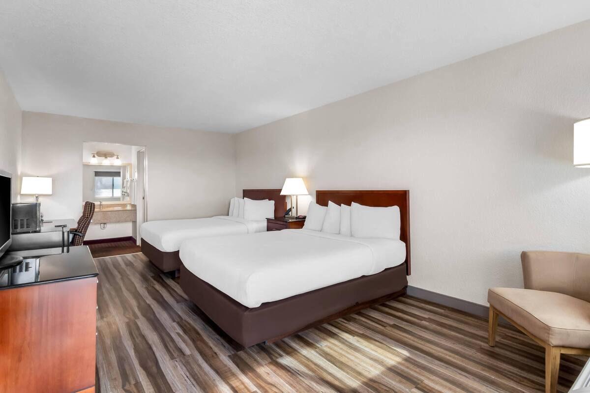 A hotel room with a large bed, a desk with a chair, a TV, and a bathroom visible through an open door.