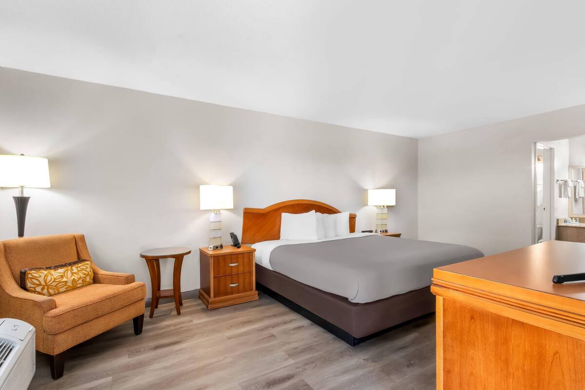 A hotel room with a bed, a chair, a nightstand, and a desk.