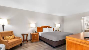 A hotel room with a bed, a chair, a nightstand, and a desk.
