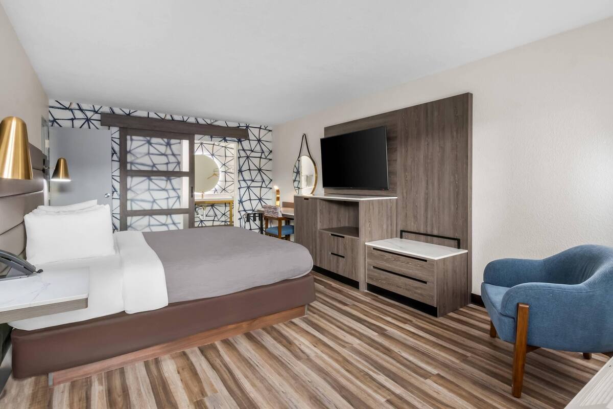 A modern hotel room with a bed, desk, TV, and a blue chair.