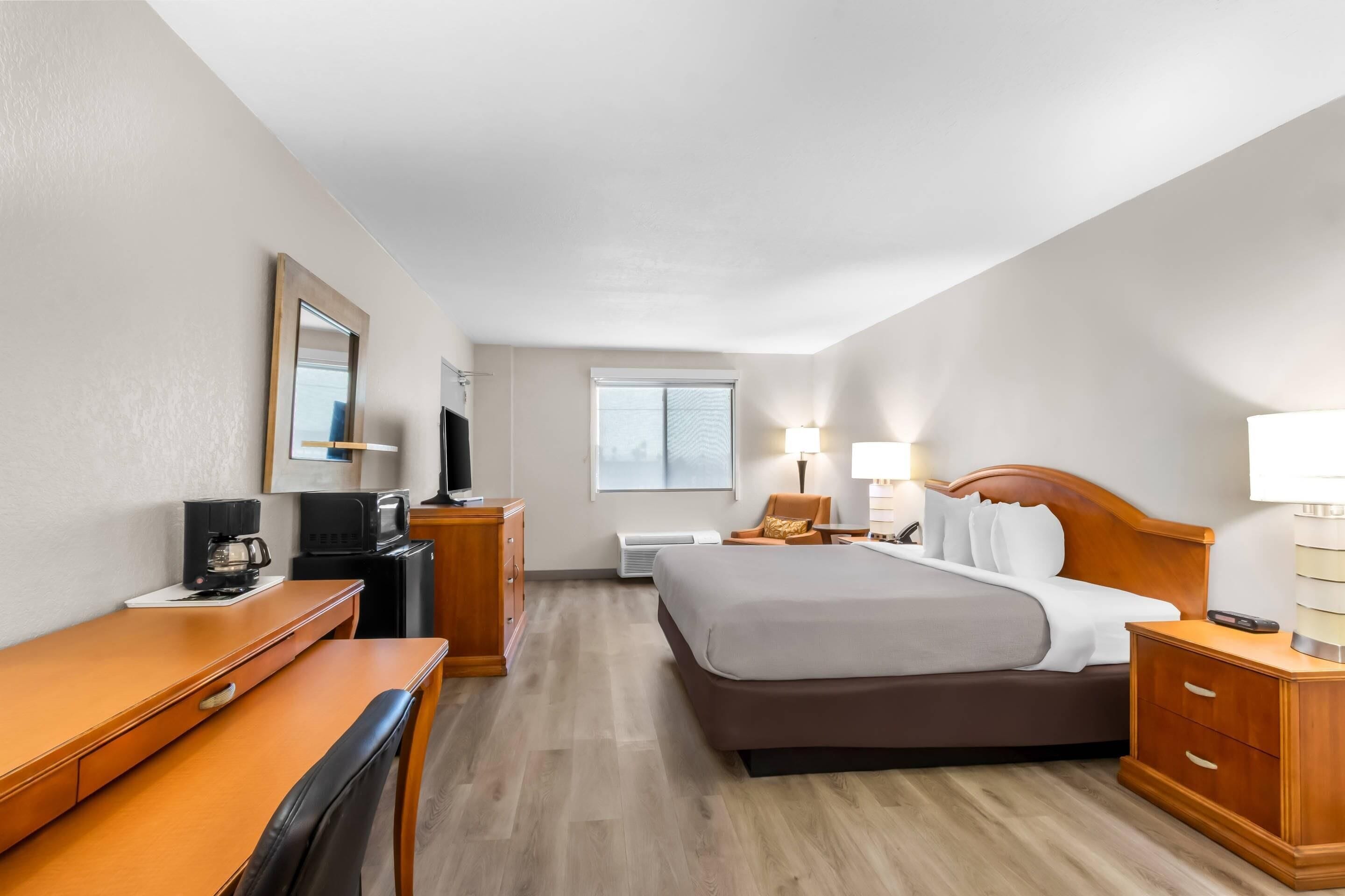 Ein Hotelzimmer mit Bett, Schreibtisch, Stuhl, Nachttischen, Lampen und einem Fernseher.