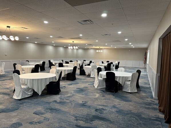 A conference room with round tables and chairs, carpeted floor, and ceiling lights.