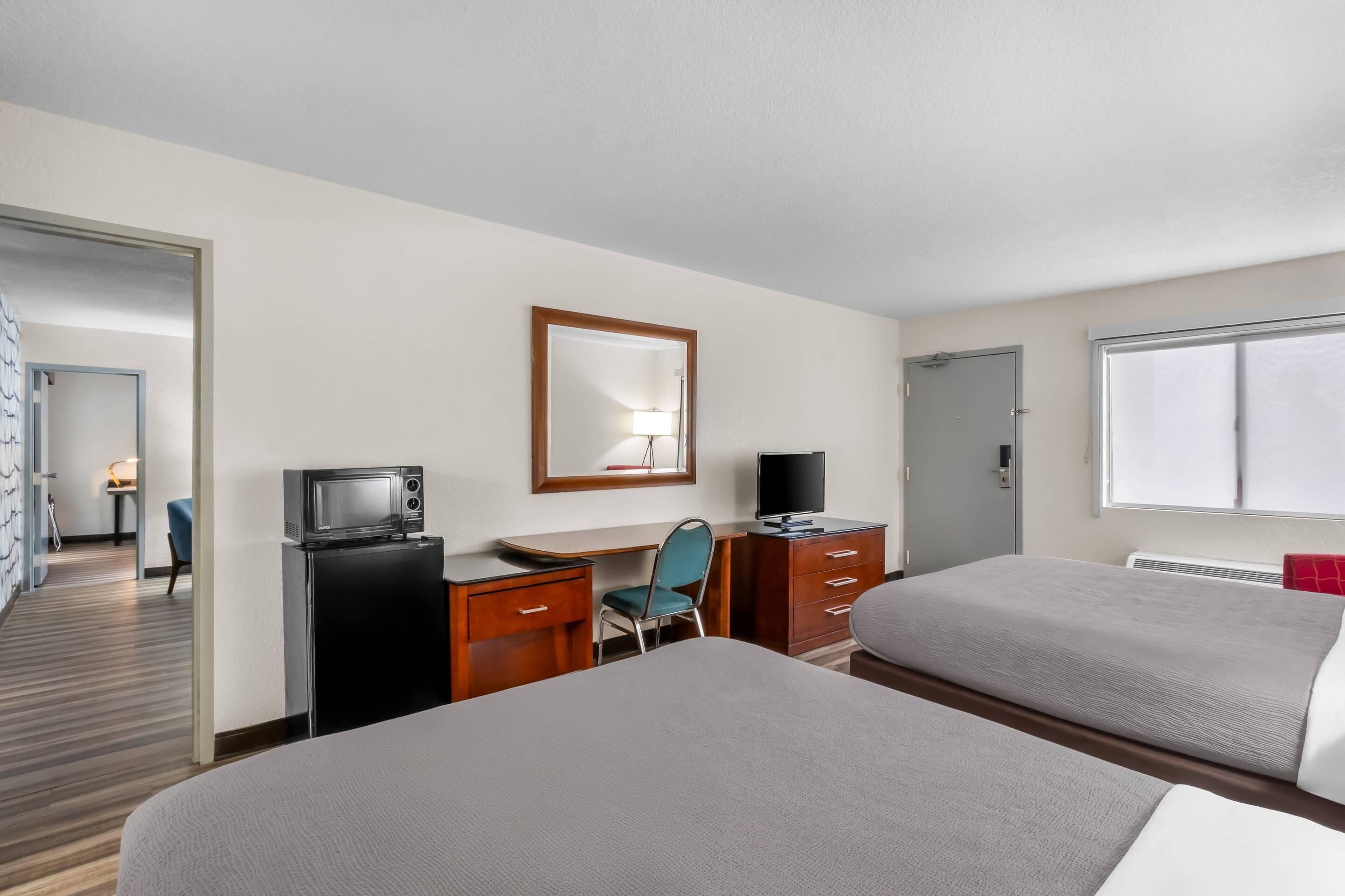 A hotel room with two beds, a desk with a computer, a TV, and a mirror.