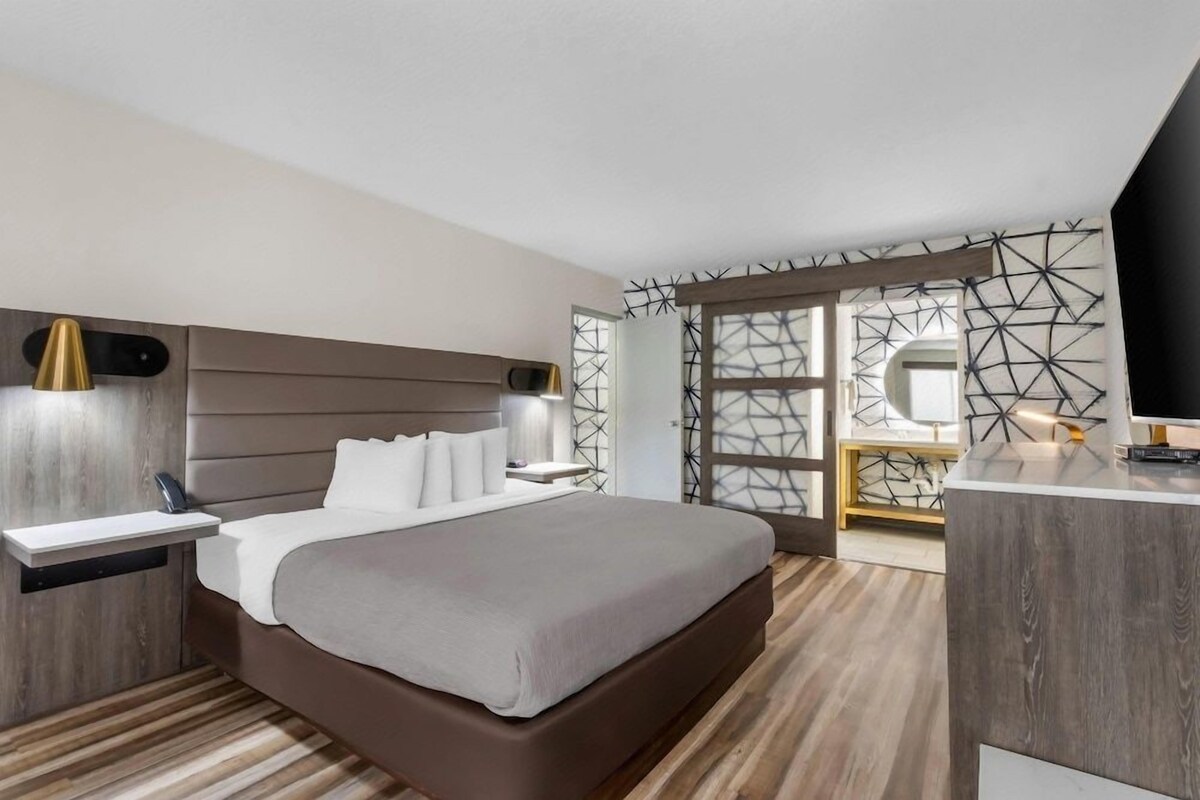 A modern hotel room with a large bed, bedside tables, a desk, and a TV.