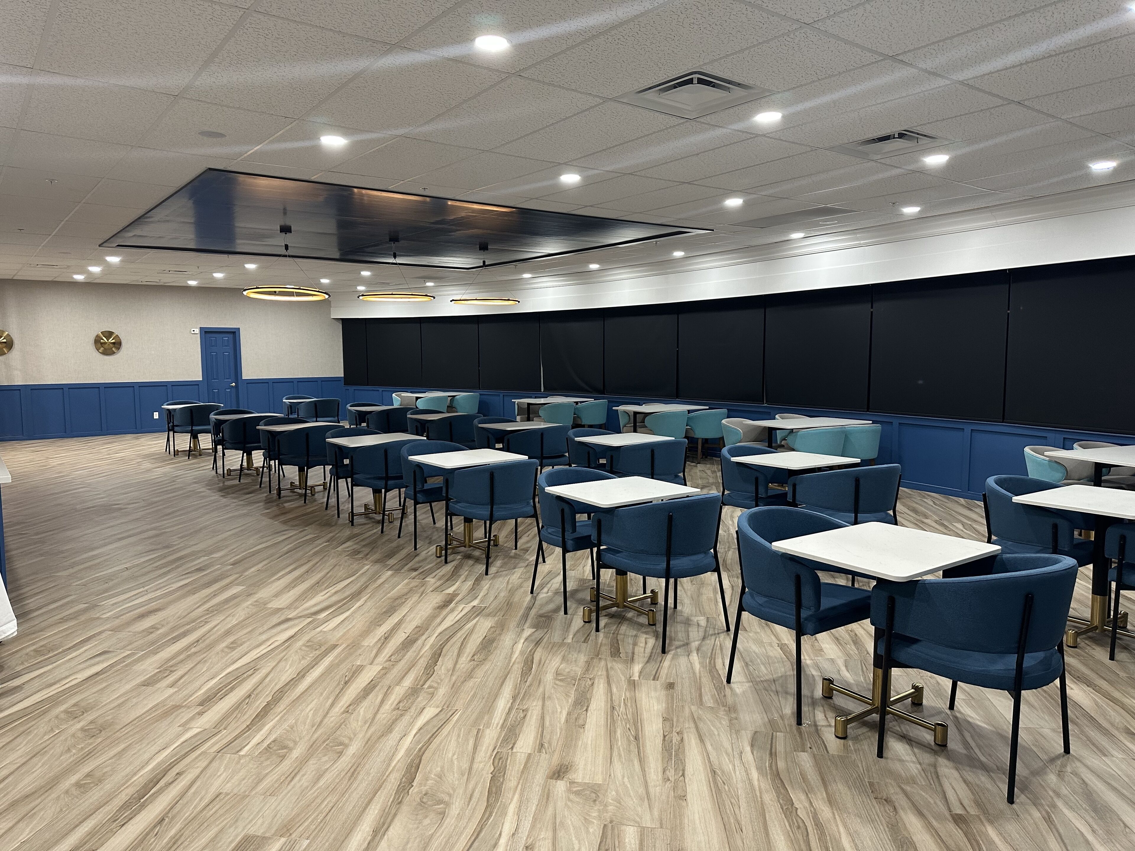 Une salle de conférence avec des rangées de tables et de chaises, un grand écran et une porte.