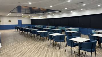 Une salle de conférence avec des rangées de tables et de chaises, un grand écran et une porte.