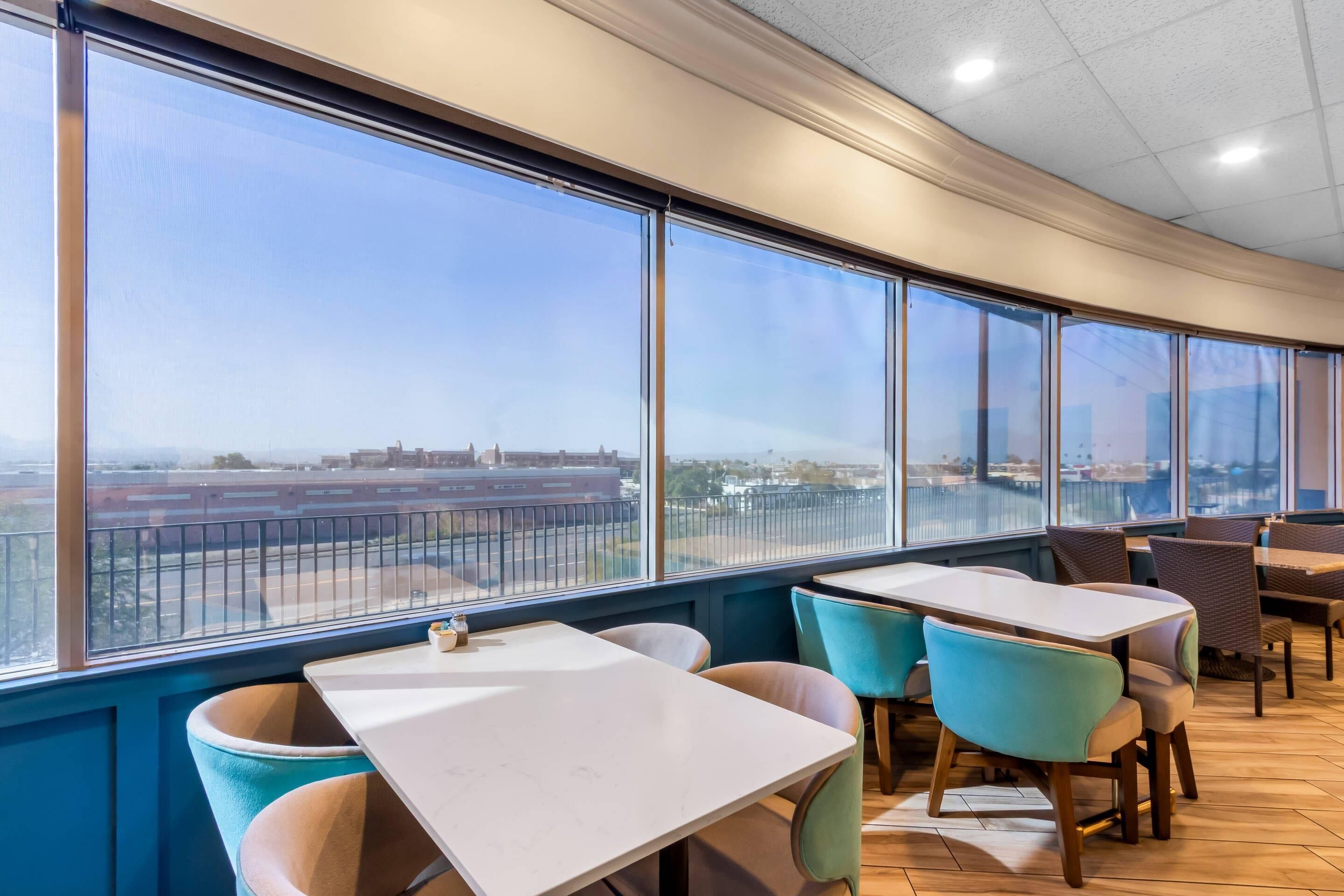 Restaurante con amplios ventanales que ofrece vistas a un aeropuerto y edificios. Mesas y sillas dispuestas para comer.