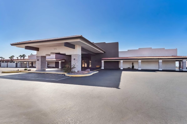 A modern hotel entrance with a covered parking area, numbered parking spaces, and a clear sky.