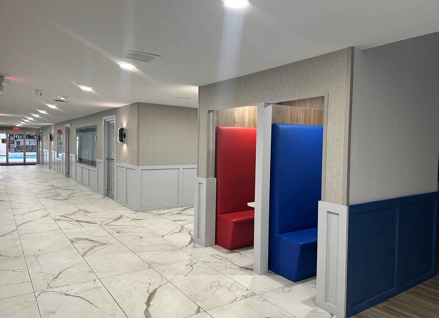 A hallway with marble flooring, red and blue seating areas, and a pool entrance.