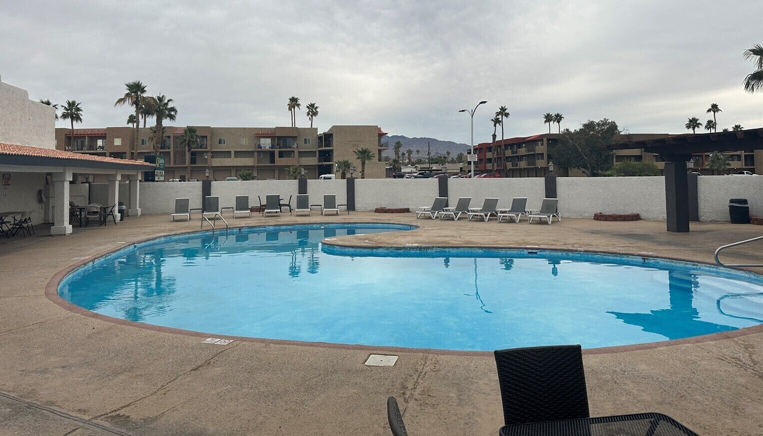 A swimming pool with lounge chairs and a view of palm trees and buildings in the background.