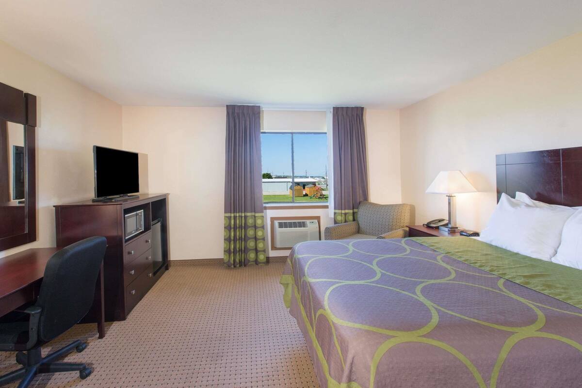 Ein Hotelzimmer mit Bett, Schreibtisch, Stuhl, Fernseher und Blick ins Freie.