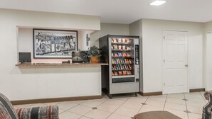 A reception area with a vending machine, a framed welcome sign, a couch, and a door.