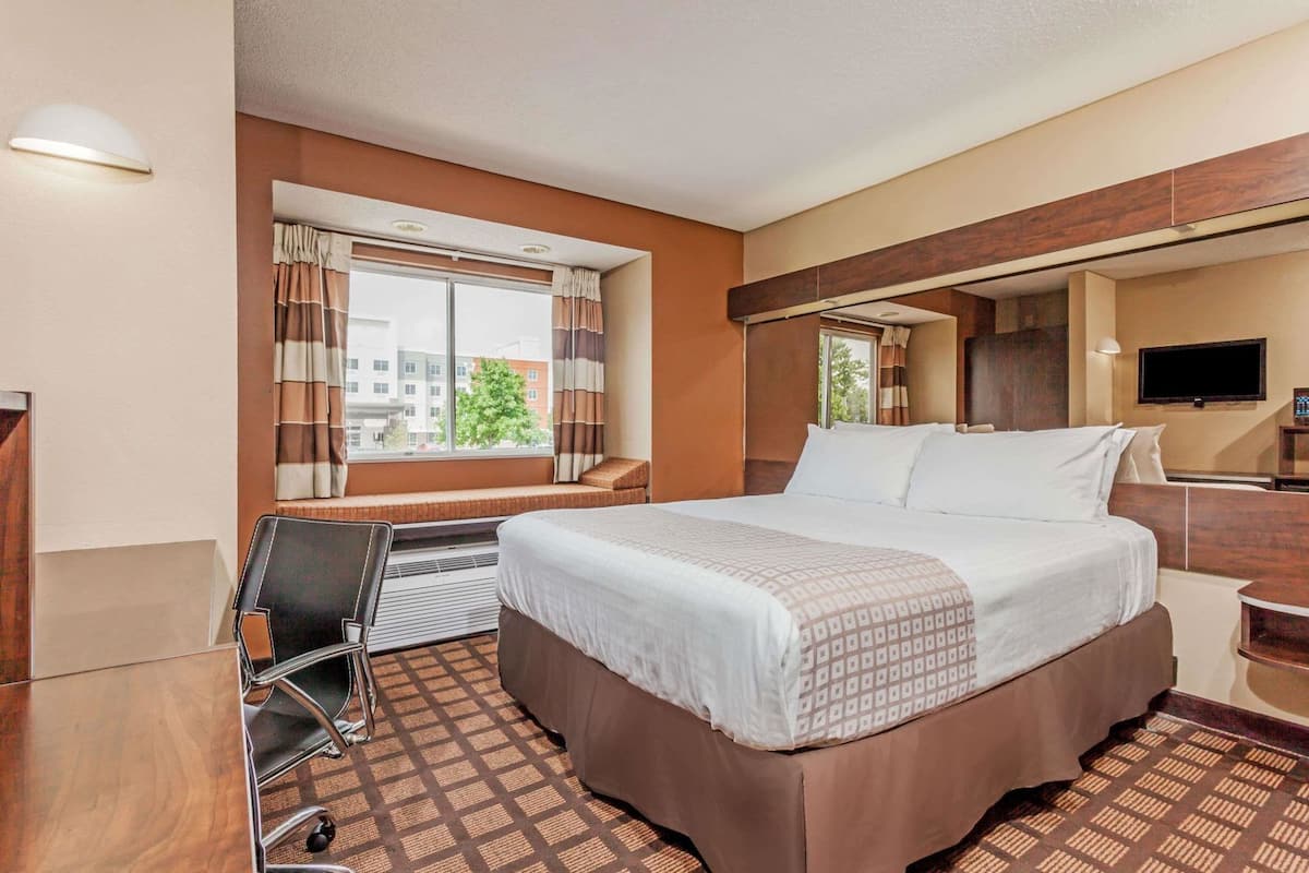 A hotel room with a bed, desk, chair, and a TV.