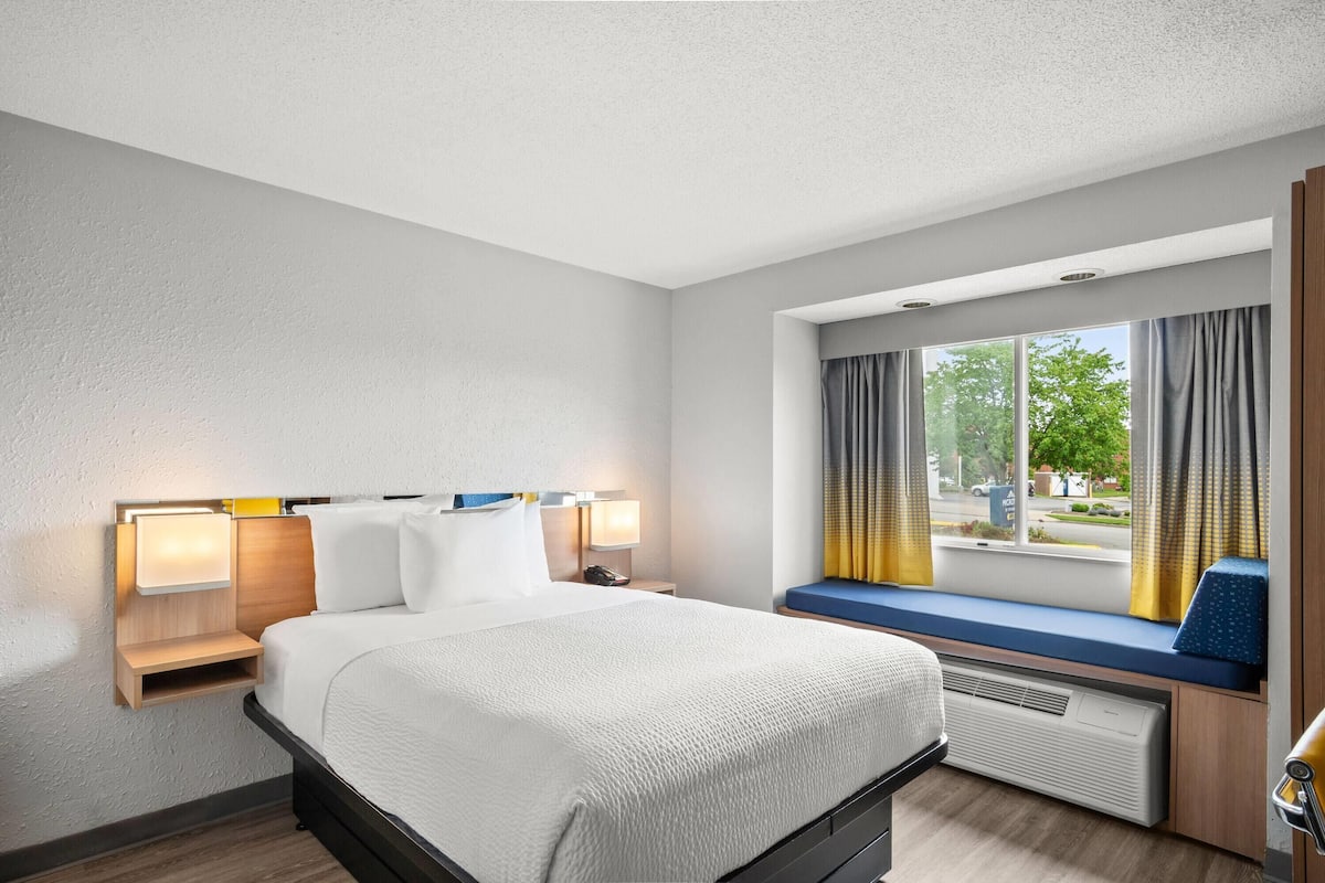 A hotel room with a bed, bedside tables, a window with curtains, and a view of the outside.